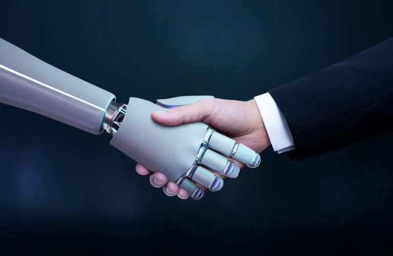 A human hand and a robotic hand meeting in a handshake, representing AI working alongside people in business.